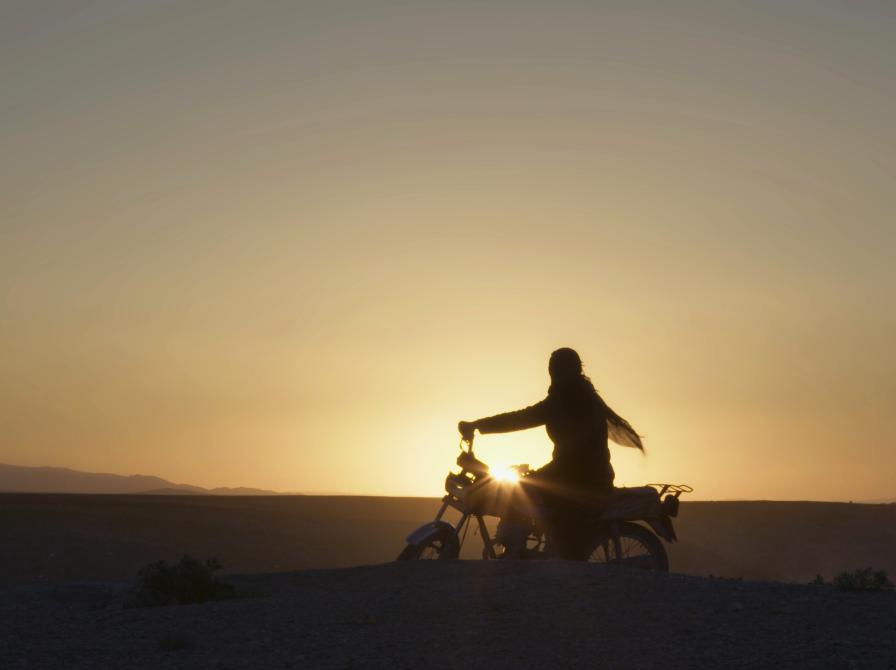 Billede af hovedpersonen fra filmen på en motorcykel i solnedgangen.